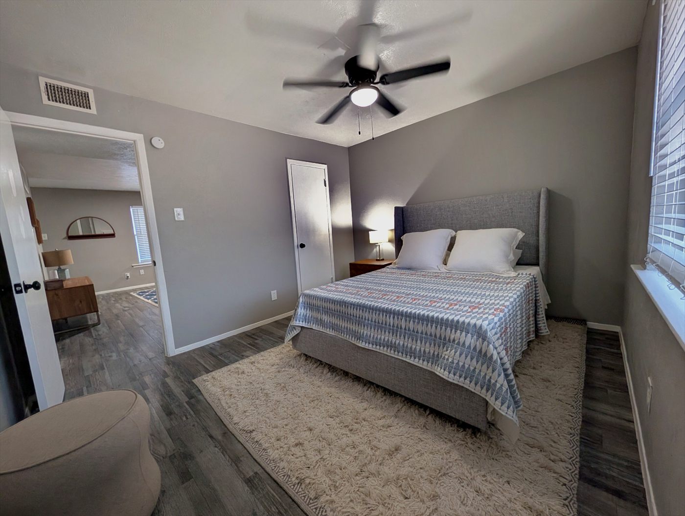 Bedroom with upholstered gray headboard, plank flooring and ceiling fan