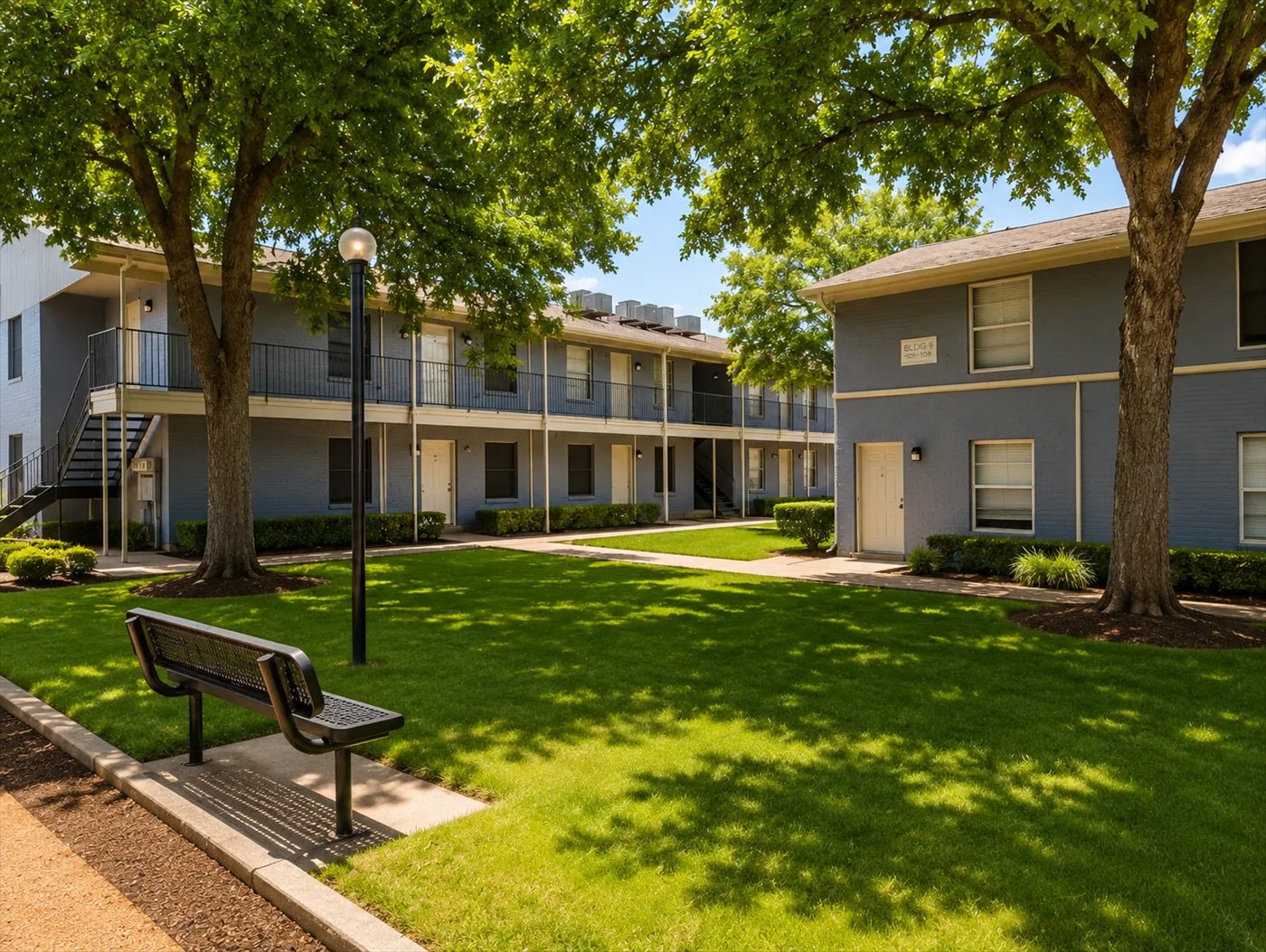 Courtyard with mature shade trees, lawn, a bench and two-story buildings