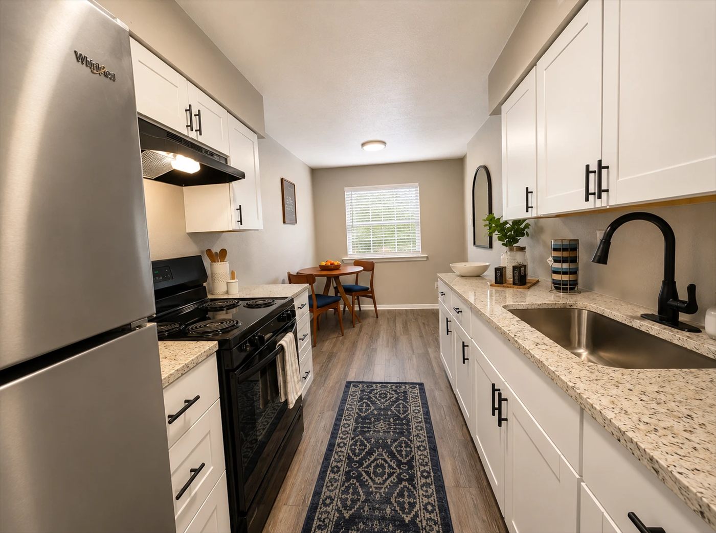 Galley kitchen with white cabinets, granite countertops, stainless refrigerator and a dining nook by the window